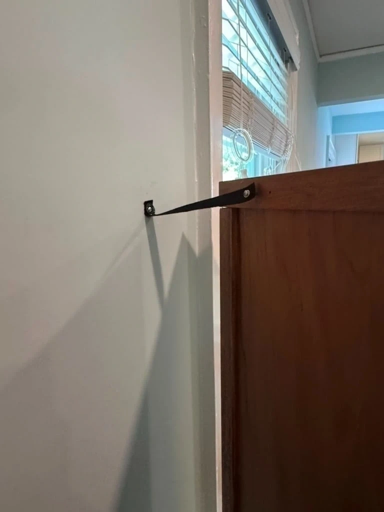 Tall wooden cabinet anchored securely to wall stud using heavy-duty anti-tip safety strap - Hastings-on-Hudson NY