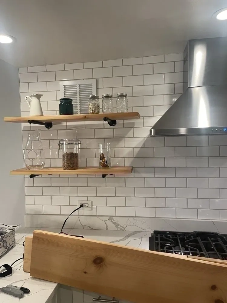 Custom natural wood floating shelves with matte black pipe brackets mounted on subway tile kitchen backsplash - Bronxville NY