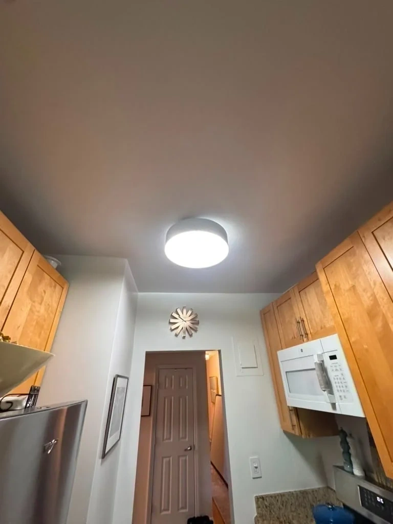 Modern white circular LED ceiling flush-mount light fixture mounted and illuminated - Rye NY