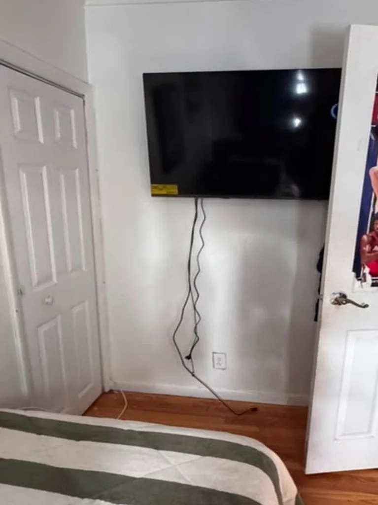 Mounted TV with loose dangling black power cords before wire concealment - Chappaqua NY