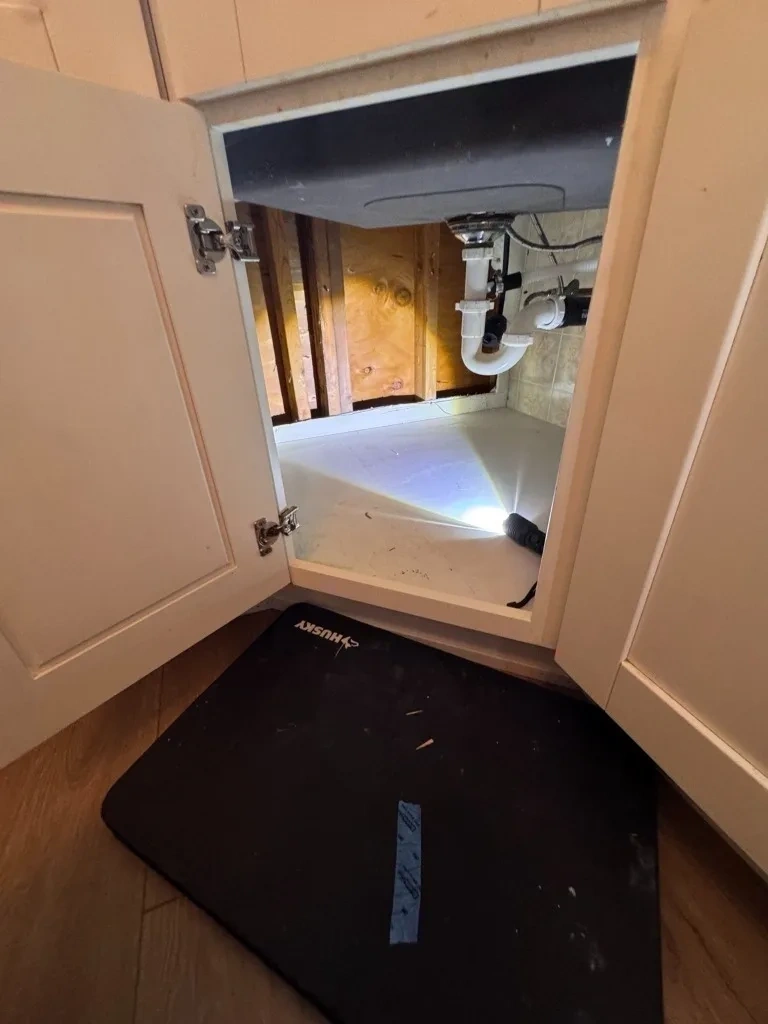 Under sink cabinet back wall cutout exposing studs before repair - Chappaqua NY